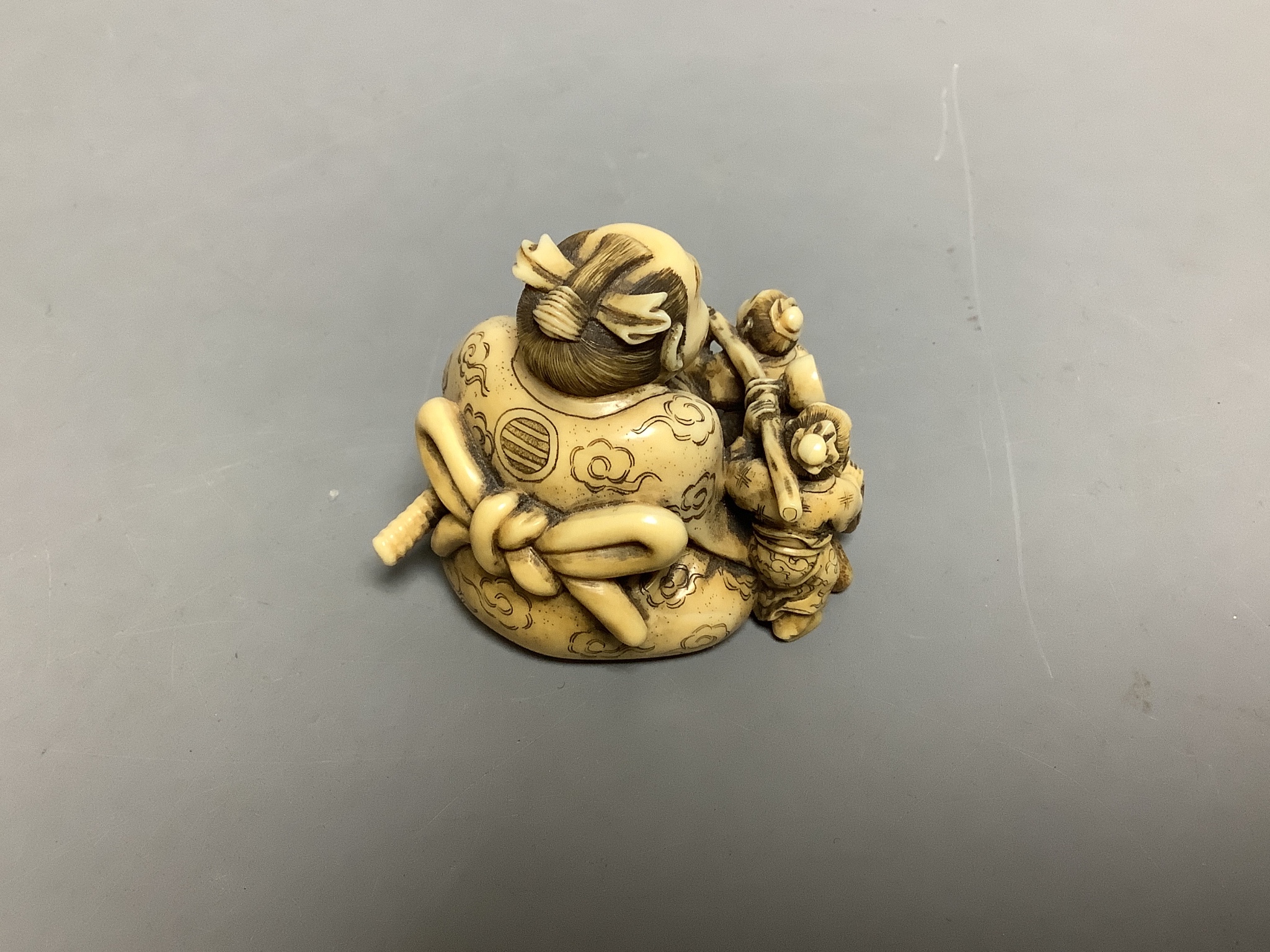 A Japanese ivory netsuke of two miniature men carrying a Samurai's tobacco pouch, Meiji period, signed